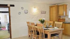 A dining area with a wooden table and chairs, a vase with flowers, and a wall clock. - Cider Cottage - E5576 (Chittlehampton, near Umberleigh)