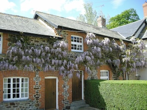 Une maison en pierre avec une porte et des fenêtres en bois, recouverte de glycines aux fleurs violettes.