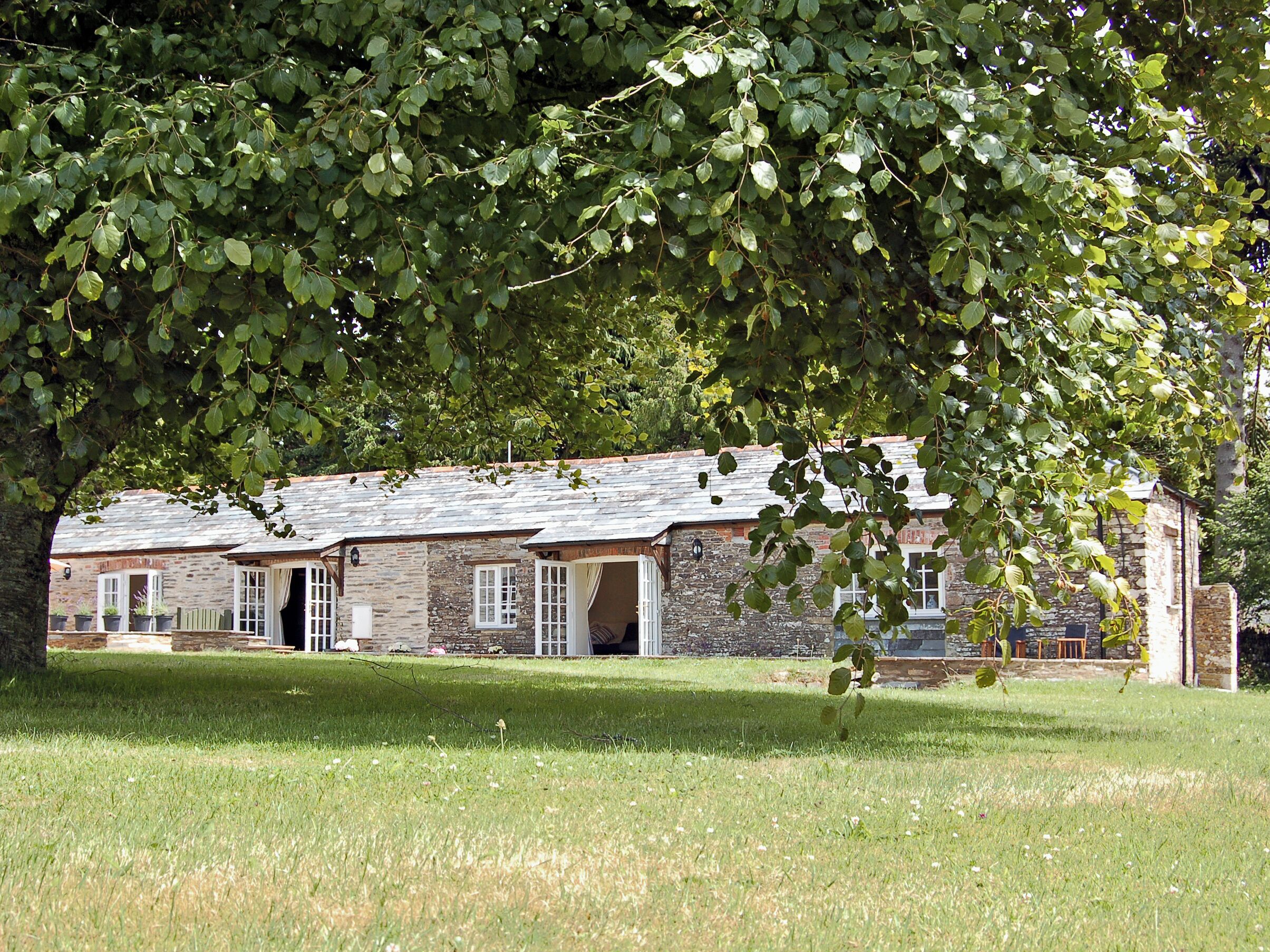 A stone building with multiple windows and doors, surrounded by a grassy area.