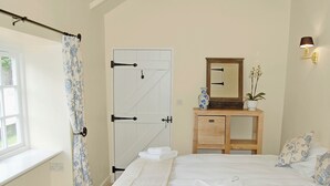 A bedroom with a bed, a wooden dresser, a mirror, and a window with a curtain. - 2 bedroom accommodation in Washaway, near Bodmin (Washaway, near Bodmin)