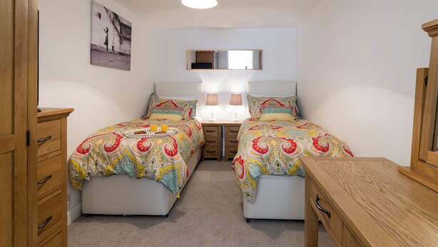 A bedroom with two beds, a bedside table, a nightstand, a lamp, a mirror, and a picture on the wall. - One Beckside Cottage (Staithes, near Whitby)