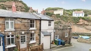 A coastal residential area with stone buildings, a wooden fence, and a clear sky. - One Beckside Cottage (Staithes, near Whitby)