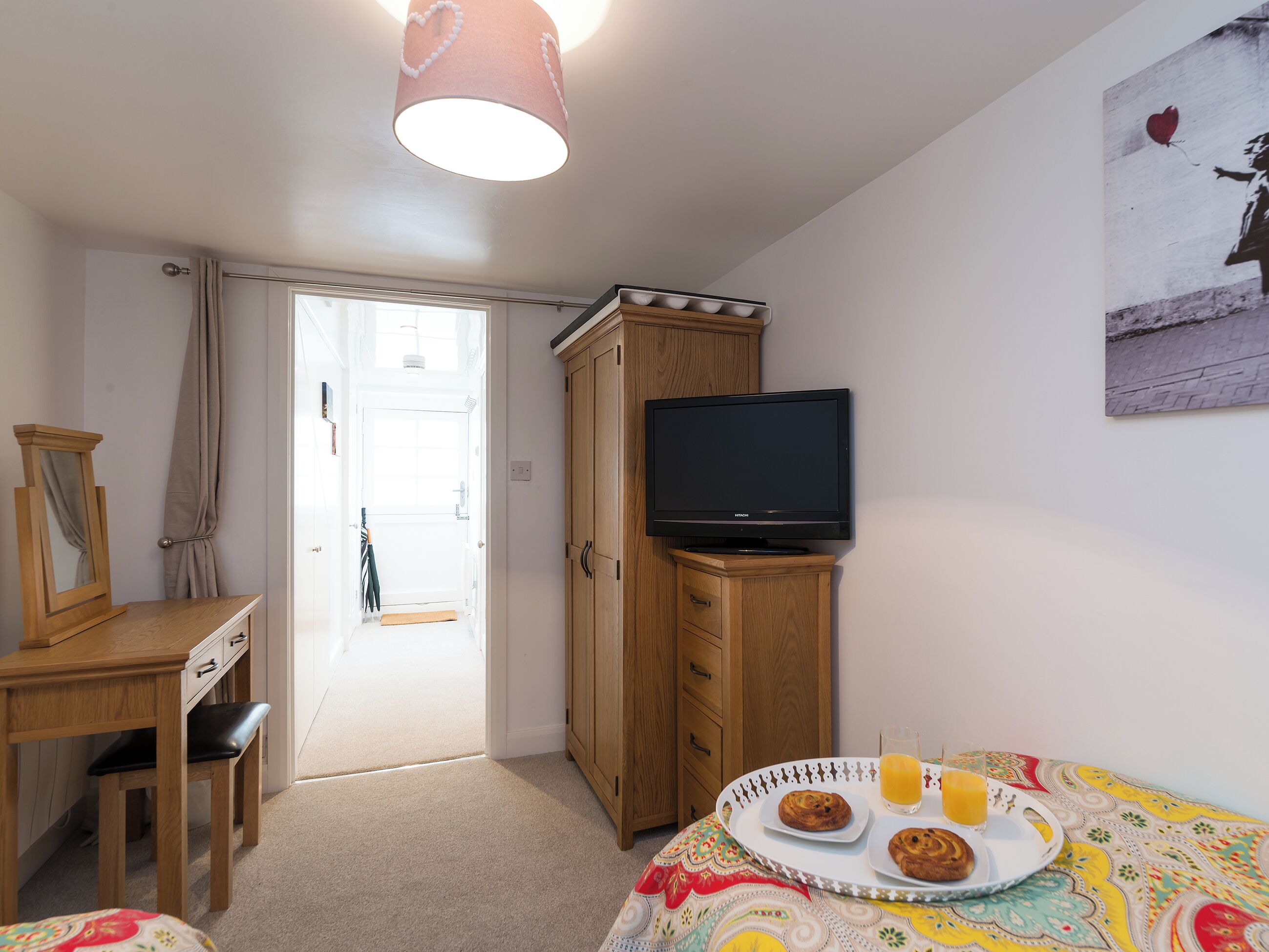 Een slaapkamer met een televisie op een houten dressoir, een bureau met stoel, en een bed met een kleurrijk beddegoed.