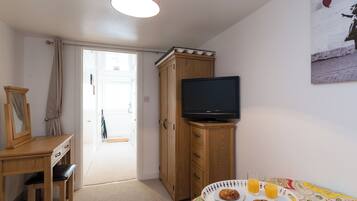 Een slaapkamer met een televisie op een houten dressoir, een bureau met stoel, en een bed met een kleurrijk beddegoed.