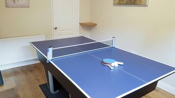 Uma mesa de pingue-pongue em um quarto com porta branca, radiador e um quadro na parede.
