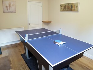 Une table de ping-pong se trouve dans une pièce avec une porte blanche, un radiateur et un tableau accroché au mur.