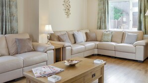 Una sala de estar con un sofá seccional color beige, una mesa de centro de madera con revistas y una lámpara.