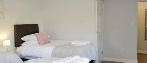 A hotel room with two beds, a nightstand, a lamp, and a door.