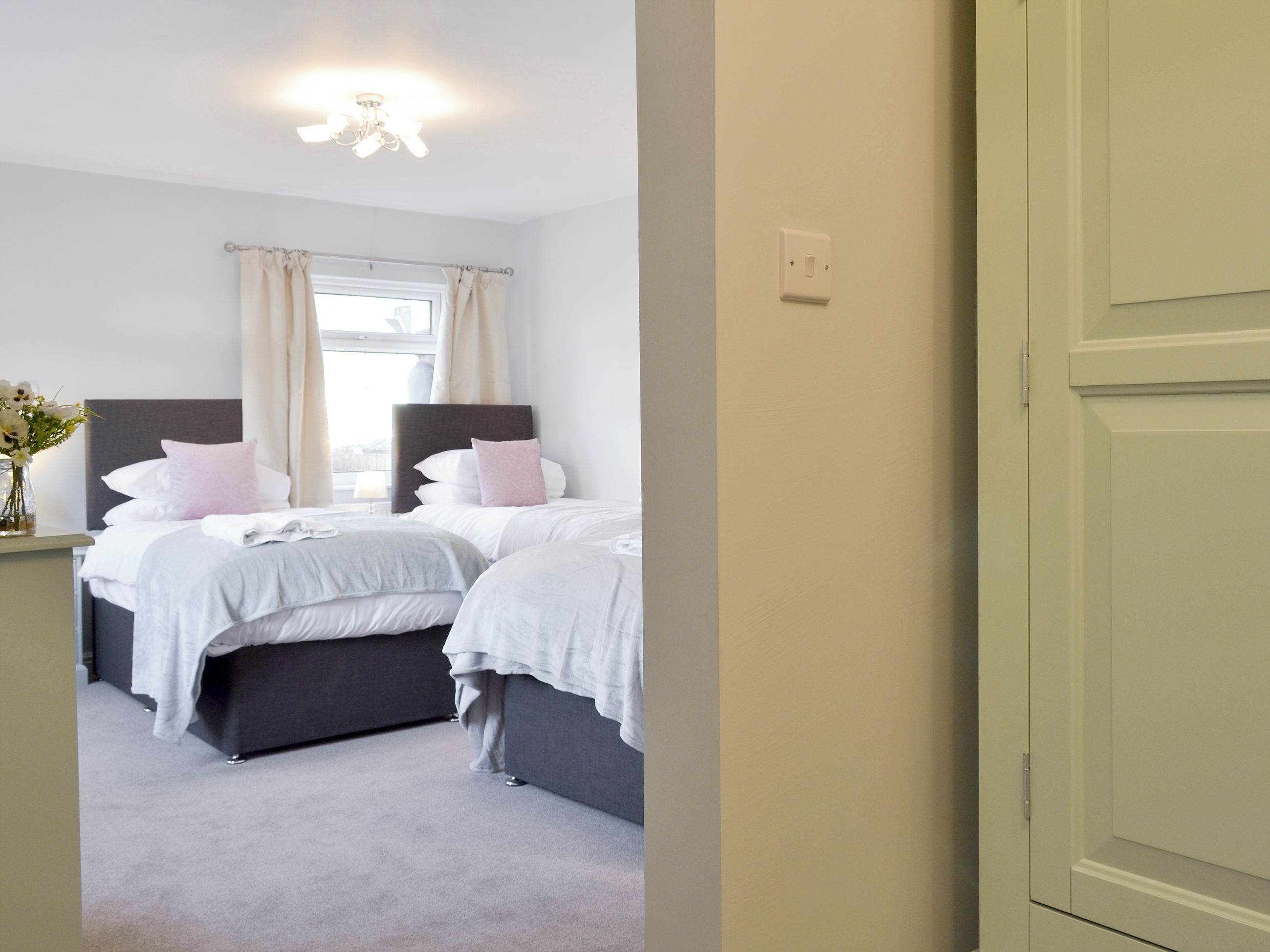 A bedroom with two beds, a nightstand, a window with curtains, and a ceiling light.