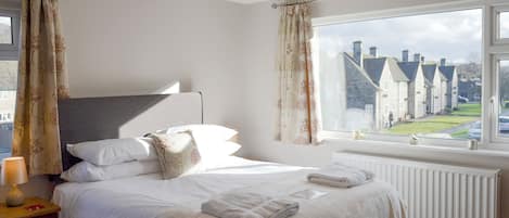 A bedroom with a bed, a nightstand, a lamp, and a window with a view of houses.