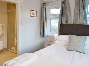 A bedroom with a bed, a bedside table with a lamp, a window with curtains, and a door leading to a bathroom.
