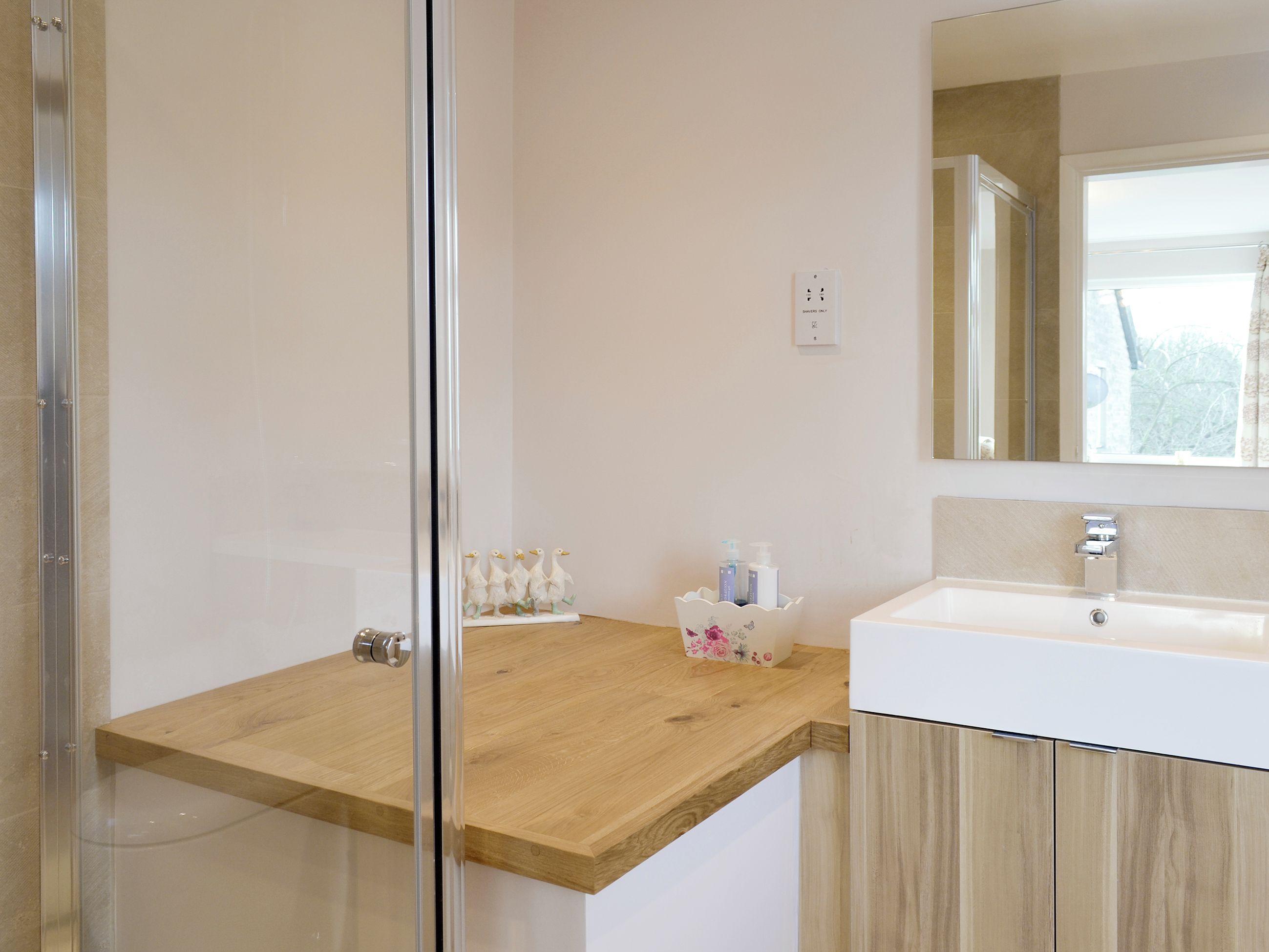 Een badkamer met een douchecabine van glas, een houten aanrechtblad, een wit wastafelmeubel en een spiegel.