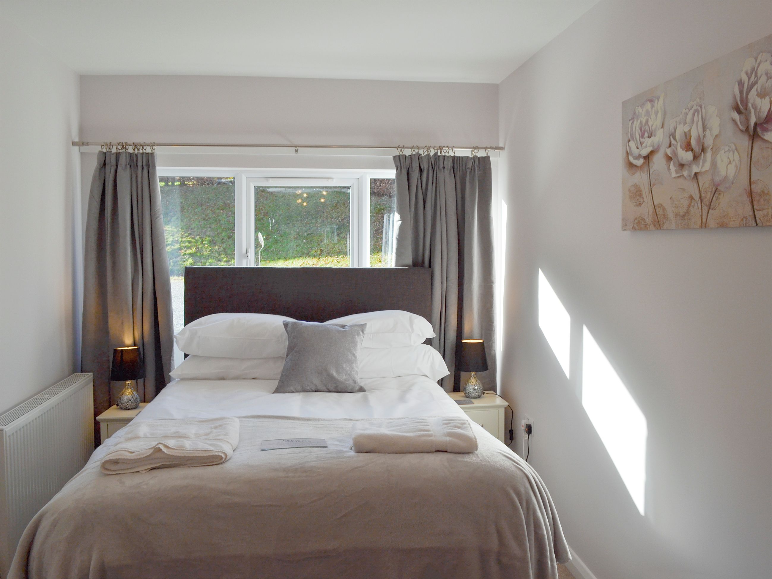 A neatly made bed with a headboard, two bedside lamps, and a window with curtains.