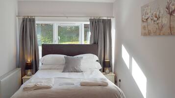A neatly made bed with a headboard, two bedside lamps, and a window with curtains.