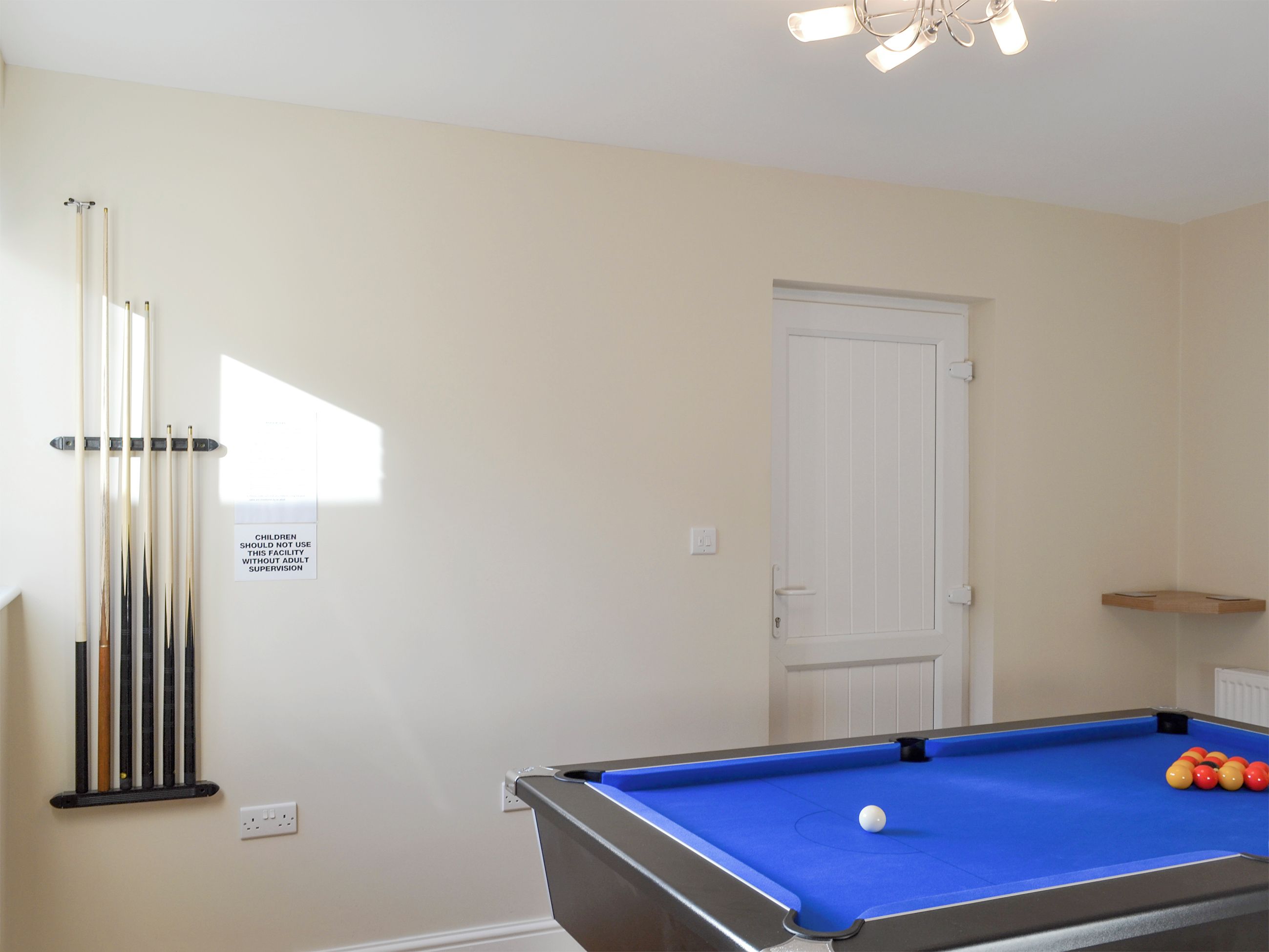 A pool table with a blue felt surface, a white door, and a sign on the wall.