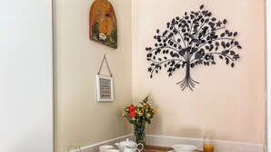 Une table en bois, des chaises blanches, un vase de fleurs et des œuvres d’art mural représentant un arbre et une horloge composent cet ensemble pour le petit-déjeuner.