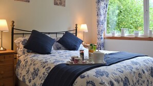 Un lit avec une literie à motifs floraux, deux lampes de chevet, un plateau avec des éléments de petit-déjeuner et une fenêtre avec des rideaux.