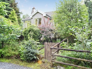 Une maison entourée d’une végétation luxuriante, avec une clôture en bois et un chemin de gravier.