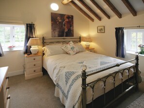 A bedroom with a four-poster bed, two bedside tables with lamps, a nightstand, a window with curtains, and a painting on the wall.