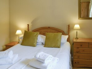 A neatly made bed with white linens and two green pillows, flanked by wooden nightstands with lamps.