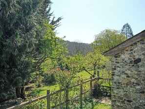 Un bâtiment en pierre, entouré d’une clôture en bois, qui offre une vue sur un paysage verdoyant parsemé d’arbres.