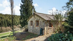 Edifici de pedra amb un petit porxo, una tanca de fusta i un jardí ple de plantes i flors.