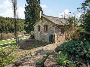 A stone building with a small porch, a wooden fence, and a garden with plants and flowers.
