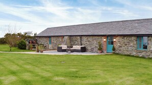 Um edifício de pedra com um alpendre coberto, área de estar ao ar livre e um gramado bem cuidado.