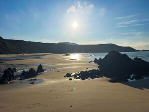 A beach with a clear sky, sun shining, and rocky formations near the shore.
