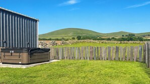 A backyard with a hot tub, a wooden fence, and a stone wall. - 2 bedroom accommodation in Llanllechid, near Bangor (Llanllechid, near Bangor)