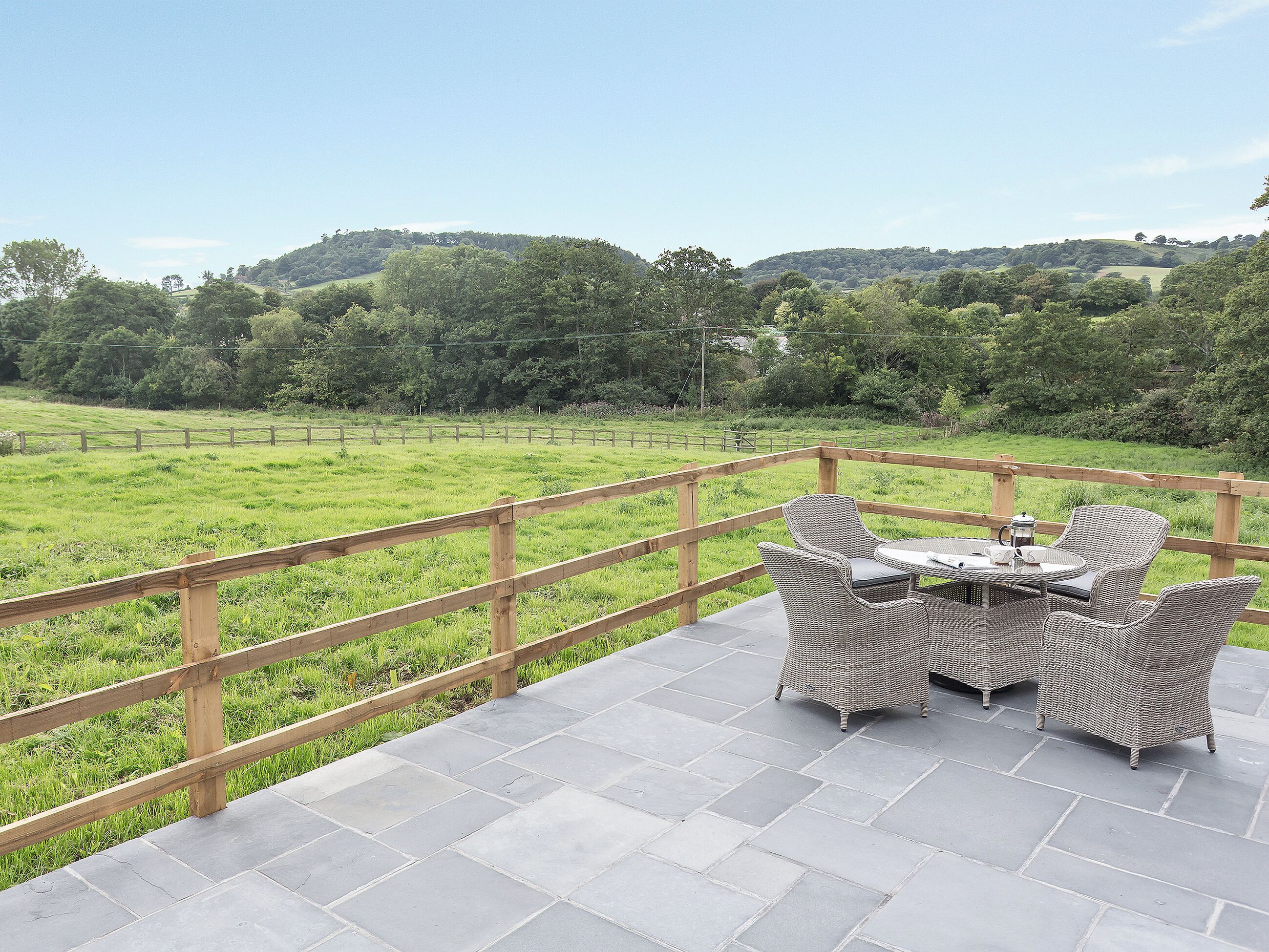 Eine Terrasse mit Korbmöbeln und Blick auf ein grünes Feld.