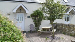 A small, cozy cottage with a stone wall, a wooden table, and a chair in the yard. - 1 bedroom accommodation in Padstow (Padstow)