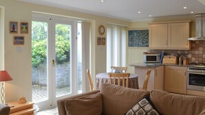 A cozy living room with a sofa and a small table, a kitchen with cabinets and appliances, and a dining area with a table and chairs. - 1 bedroom accommodation in Padstow (Padstow)