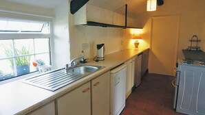 A compact kitchen with a sink, stove, and a window with plants. - 1 bedroom accommodation in Cilan, near Abersoch (Cilan, near Abersoch)