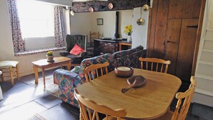 A cozy living room with a wooden dining table, a patterned sofa, and a comfortable armchair. - 1 bedroom accommodation in Cilan, near Abersoch (Cilan, near Abersoch)