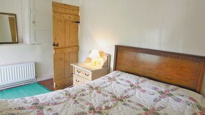 A bedroom with a wooden bed, a nightstand with a lamp, a wooden wardrobe, and a radiator. - 1 bedroom accommodation in Cilan, near Abersoch (Cilan, near Abersoch)