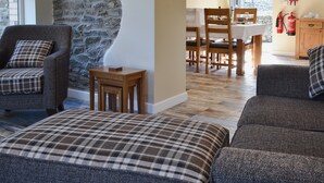 A cozy living room with a stone wall, a dining area with wooden furniture, and a kitchen area with a fire extinguisher. - 2 bedroom accommodation in Cilcennin, near Aberaeron (Cilcennin, near Aberaeron)