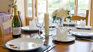 A dining table set with plates, glasses, a bottle, and a candle, with a window view. - 2 bedroom accommodation in Carmarthen (Carmarthen)