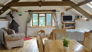 A cozy loft bedroom with exposed wooden beams, a fireplace, a television, and a large window with curtains. - 2 bedroom accommodation in Ugborough, Ivybridge (Ugborough, Ivybridge)