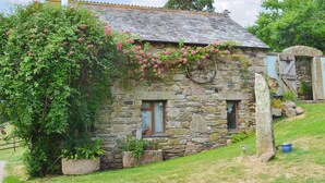 A stone house with a tiled roof, a chimney, and a wheel mounted on the wall. - 2 bedroom accommodation in Ugborough, Ivybridge (Ugborough, Ivybridge)