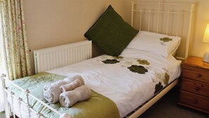 A neatly made bed with a green pillow, a bedside table with a lamp, and floral curtains. - 2 bedroom accommodation in Charlestown, St Austell (Charlestown, St Austell)