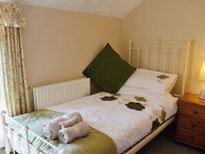 A neatly made bed with a green pillow, a bedside table with a lamp, and floral curtains.