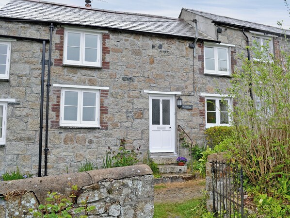 A stone building with multiple windows and a door, surrounded by greenery and a stone wall.