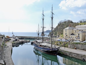 A historic sailing ship docked at a harbor with a building and a road nearby.
