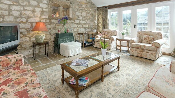 A cozy living room with a stone wall, a television, a fireplace, and floral furniture. - Bickley School Annexe (Bickley, near Langdale End)
