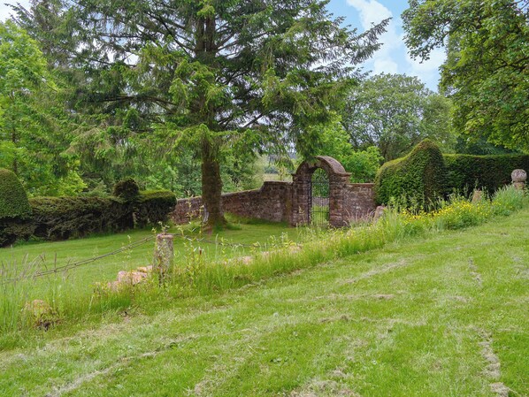A historic stone archway leading into a lush garden with mature trees and a well-maintained lawn.