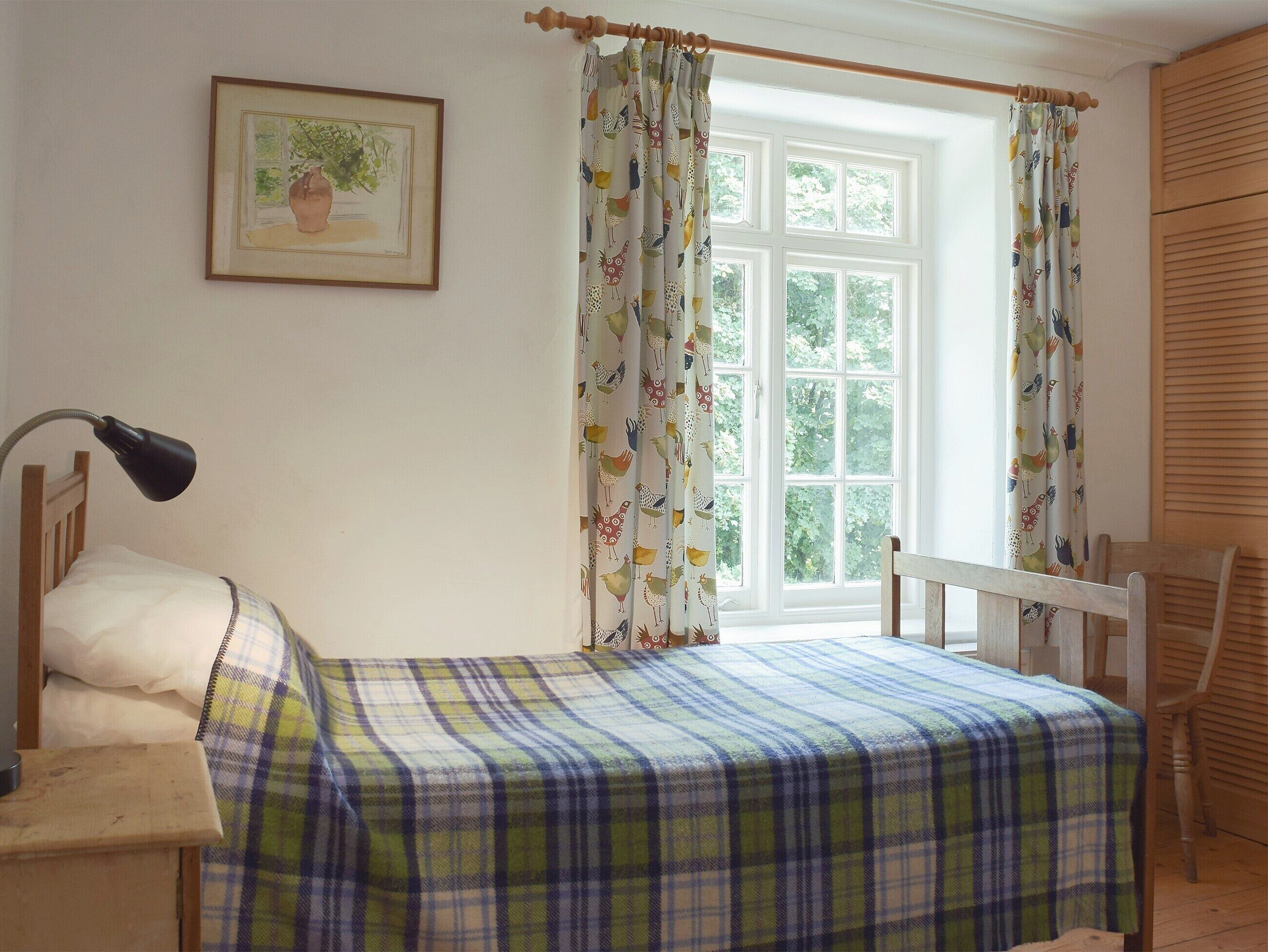 Ein Schlafzimmer mit einem Bett, einem Schreibtisch, einem Stuhl, einem Fenster mit Vorhängen und einem gerahmten Bild an der Wand.