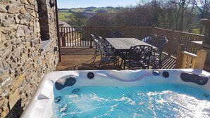 A hot tub on a wooden deck with stone walls, surrounded by outdoor furniture and a scenic view. - 4 bedroom accommodation in Mydroilyn, near Aberaeron (Mydroilyn, near Aberaeron)