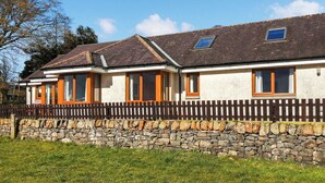 A two-story house with a stone wall foundation, multiple windows with orange frames, and a wooden fence.