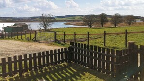 A fenced area with a body of water, trees, and a distant view of hills.